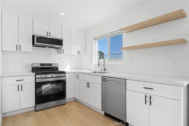 a kitchen with stainless steel appliances granite countertop a sink dishwasher a stove and a refrigerator with wooden floor