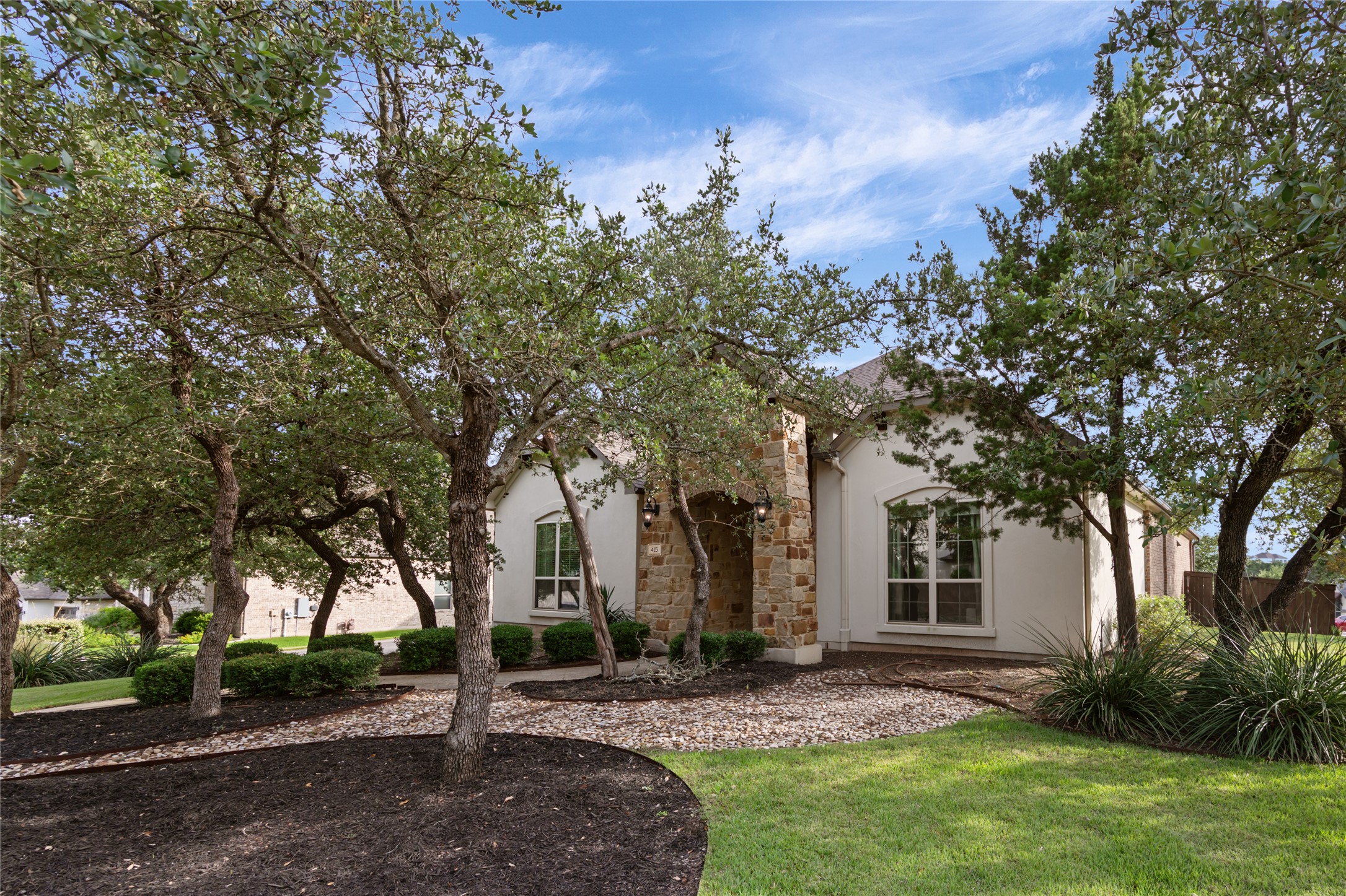 Mature trees and inviting landscaping frame the attractive stone and stucco facade of this welcoming residence.