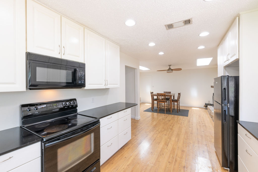 5310 Presidio Road Austin, TX 78745 - Photo 7 of 34 A well-appointed kitchen boasts sleek black appliances and ample white cabinetry, flowing into a spacious dining area with hardwood floors.