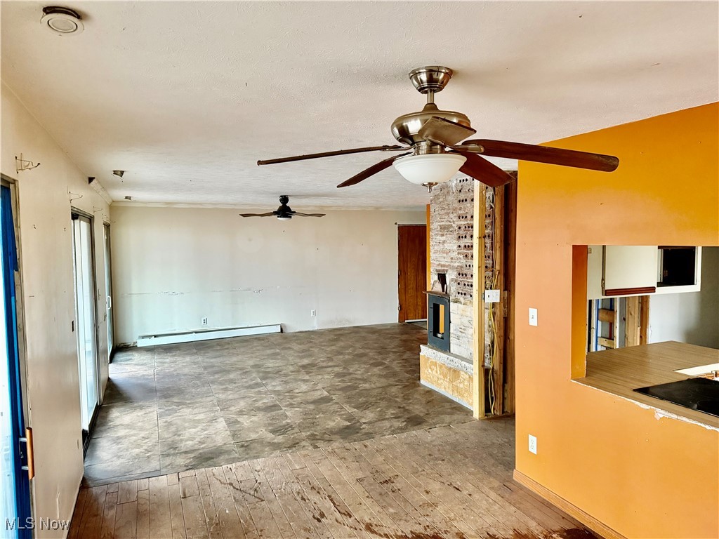 2898 Canton Road Uniontown, OH 44685 - Photo 11 of 20 Unfurnished living room featuring hardwood / wood-style floors, baseboard heating, ceiling fan, a large fireplace, and a textured ceiling