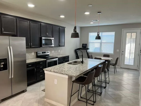 a kitchen with stainless steel appliances granite countertop a stove a refrigerator a sink a dining table and chairs