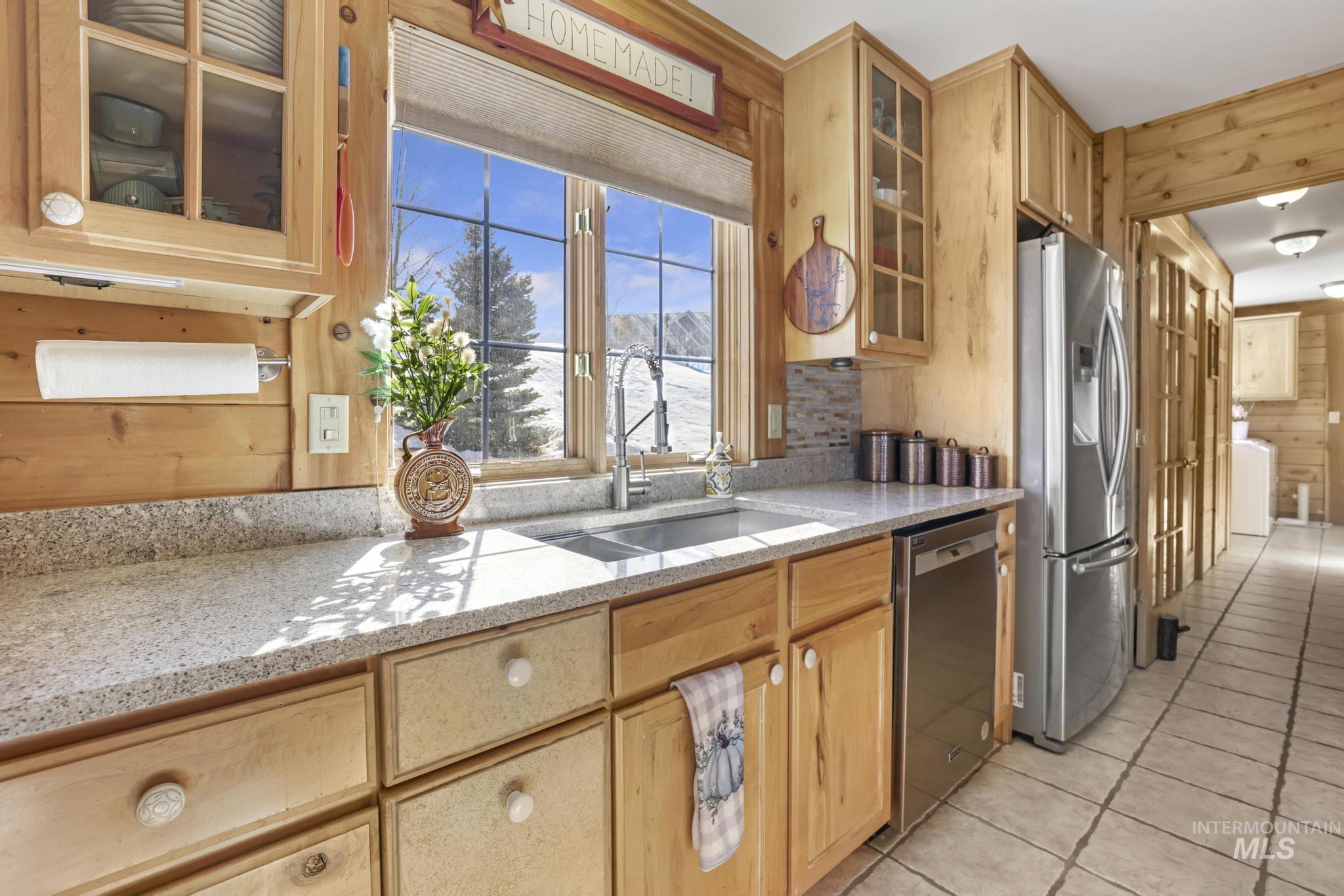 203 North Brush Road Fairfield, ID 83327 - Photo 16 of 50 Kitchen featuring wooden walls, appliances with stainless steel finishes, light stone countertops, light tile patterned floors, and glass insert cabinets