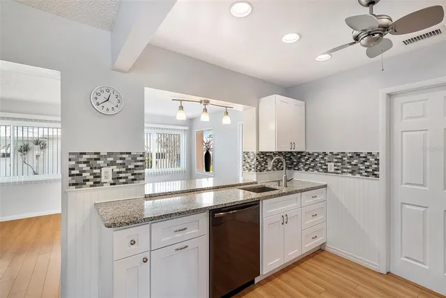 a kitchen with a sink dishwasher and white cabinets with wooden floor