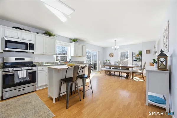 a kitchen with stainless steel appliances kitchen island granite countertop a stove top oven a sink a dining table and chairs with wooden floor