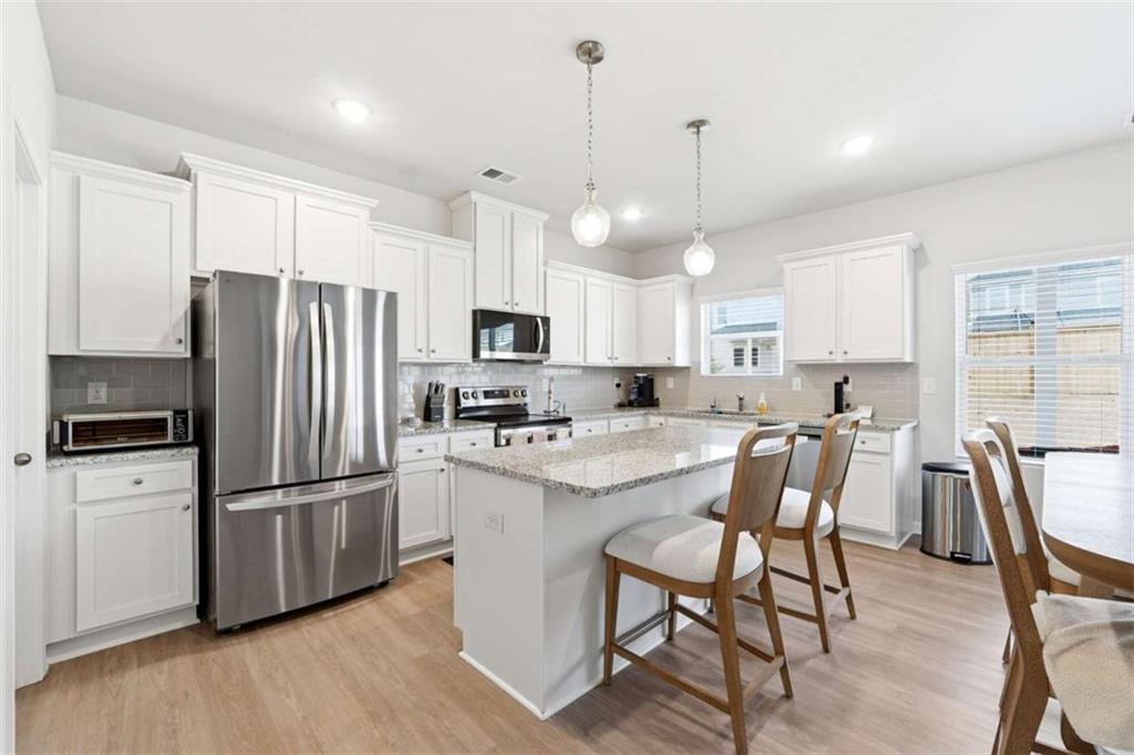 11817 Rizvan Place Covington, GA 30014 - Photo 11 of 40 a kitchen with stainless steel appliances a refrigerator a stove a sink a dining table and chairs with wooden floor