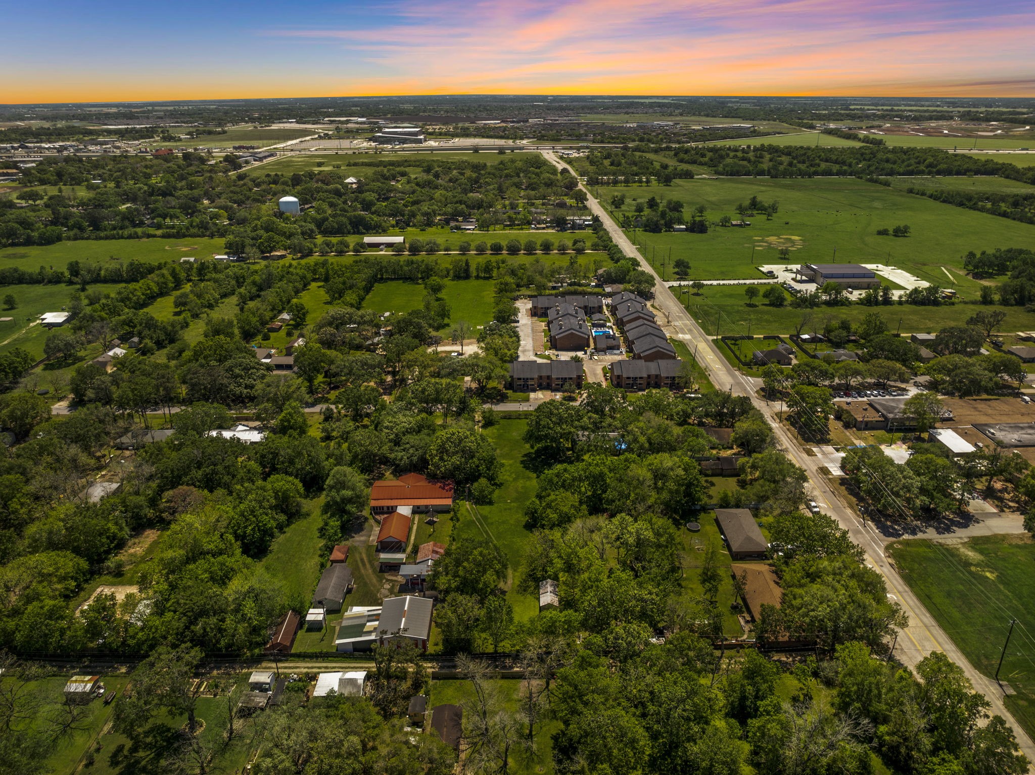 903 Brooks Avenue Rosenberg, TX 77471 - Photo 3 of 11 Sweeping sunset views showcase the full expanse of this tree-lined parcel, framed by nearby development and infrastructure—a compelling canvas for new construction.