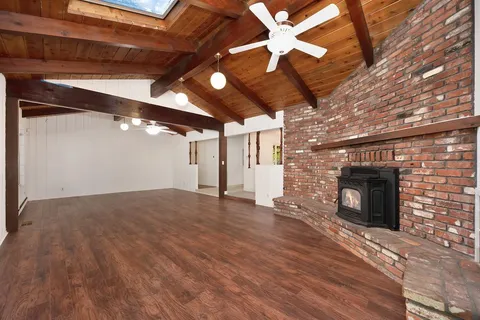 a view of an empty room with wooden floor fireplace and a window