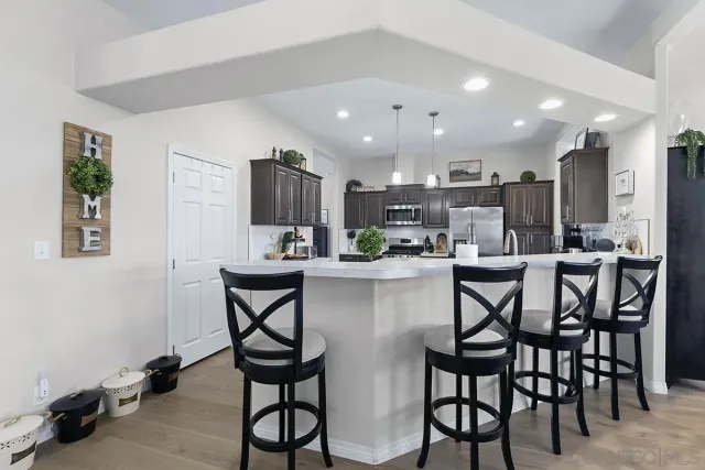 a kitchen with stainless steel appliances kitchen island granite countertop a dining table chairs and a refrigerator