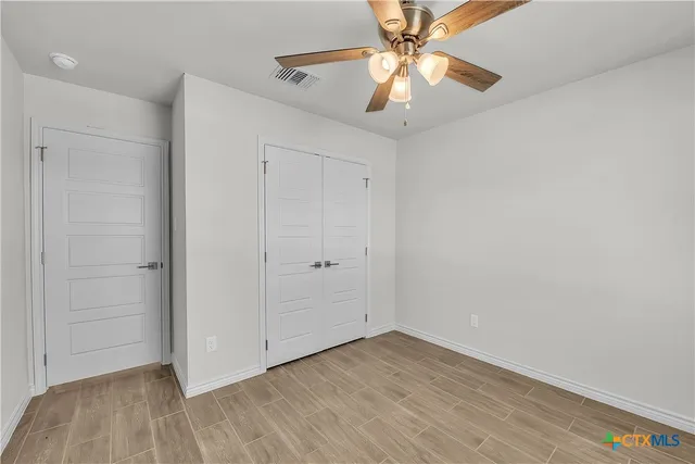 an empty room with wooden floor a ceiling fan and closet area