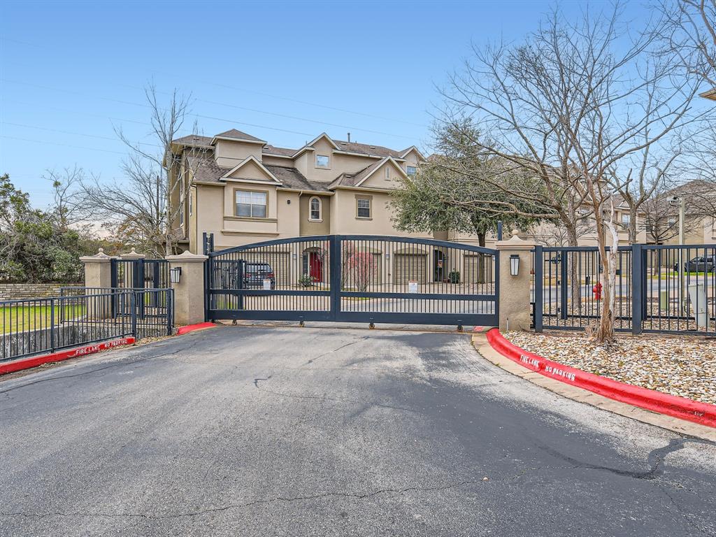 11203 Ranch Road 2222, Unit 2404 Austin, TX 78732 - Photo 18 of 28 Gated entry featuring iron gates and stone pillars, providing access to multi-story residences with stucco exteriors and arched windows