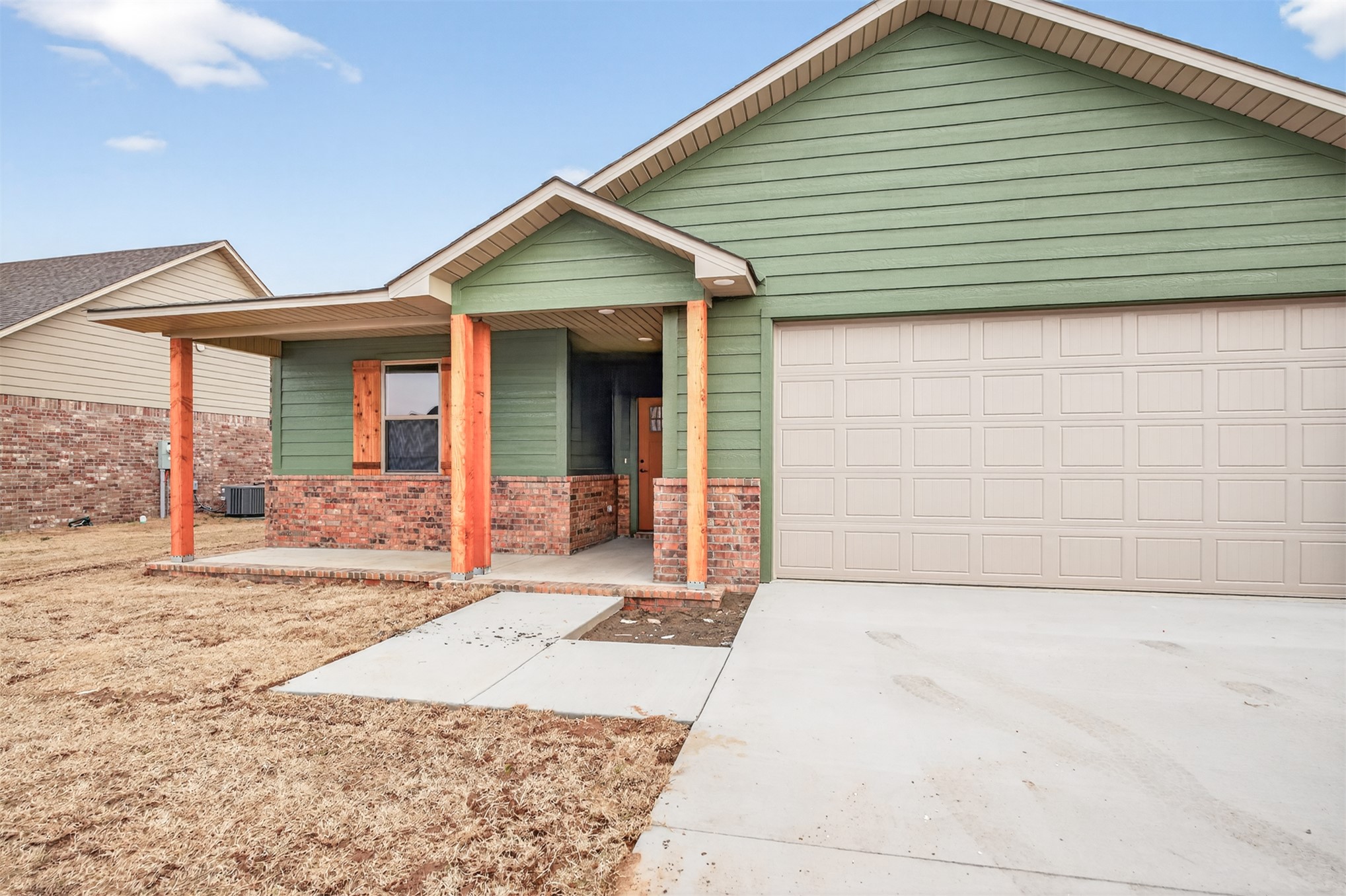 124 Countryside Way Pocola, OK 74902 - Photo 37 of 39 Green siding exterior with brick accents, covered front porch with wood-finish posts, and an attached garage