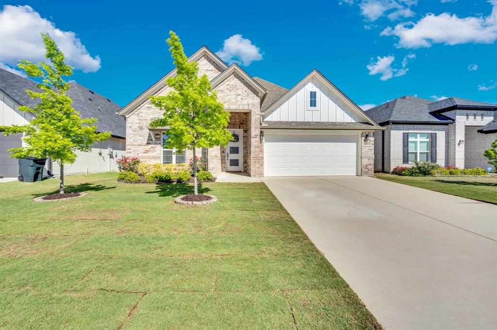 View of front of property with board and batten siding, concrete driveway, a front lawn, a garage, and brick siding