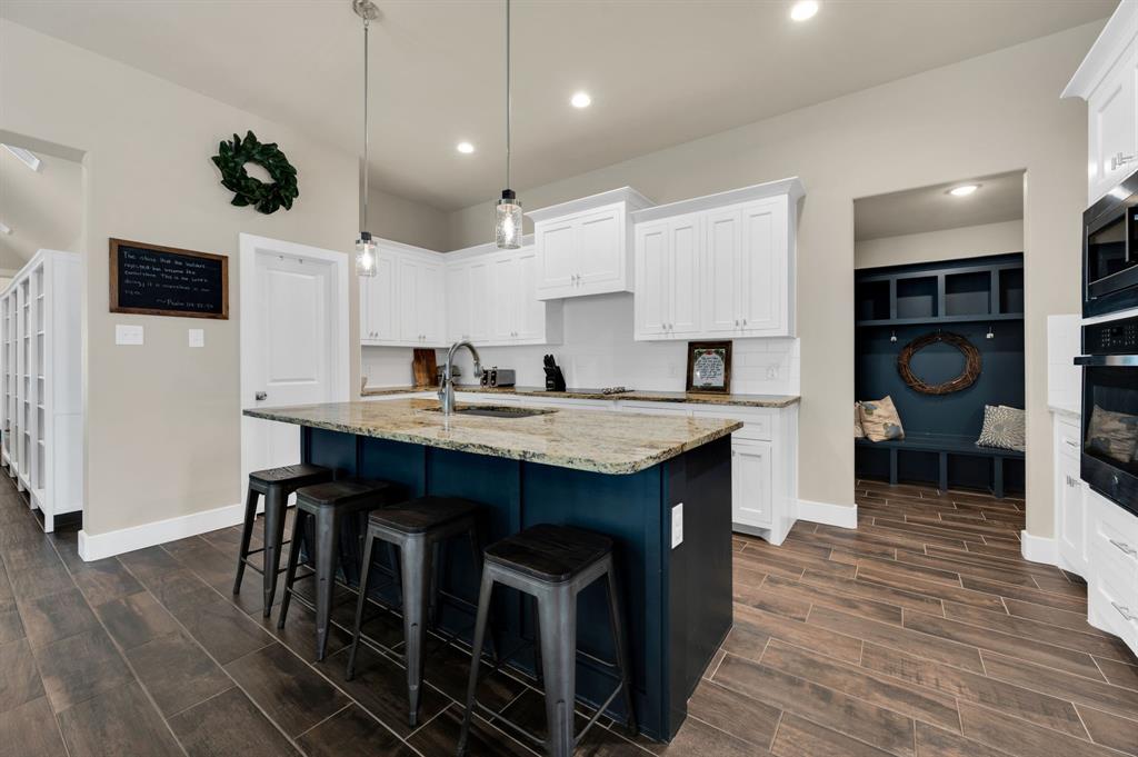 1313 Ridgeview Drive Weatherford, TX 76086 - Photo 10 of 34 Two tone kitchen featuring a breakfast bar, a kitchen island with sink, wood finish floors, light stone countertops, and two tone cabinets