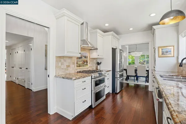 a kitchen with stainless steel appliances granite countertop a stove top oven a refrigerator a sink dishwasher and white cabinets with wooden floor