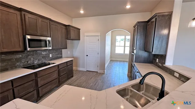 a kitchen with stainless steel appliances granite countertop a refrigerator a stove top oven a sink dishwasher and wooden cabinets with wooden floor
