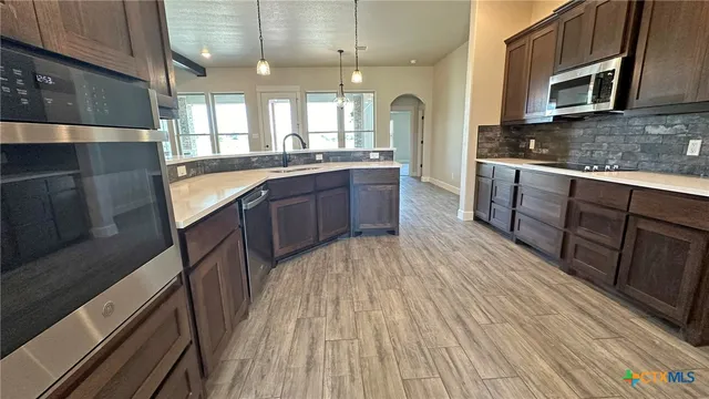 a large kitchen with stainless steel appliances wooden floors wooden cabinets a microwave and a sink
