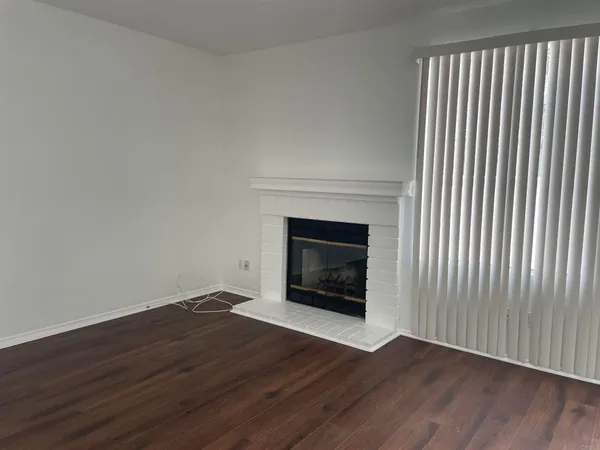 a view of an empty room with wooden floor fireplace and a window