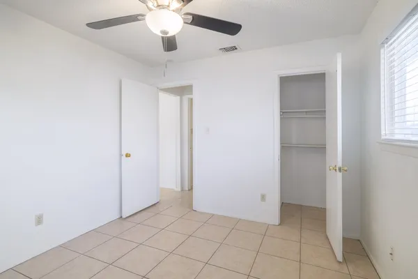 a view of an empty room with window and chandelier fan