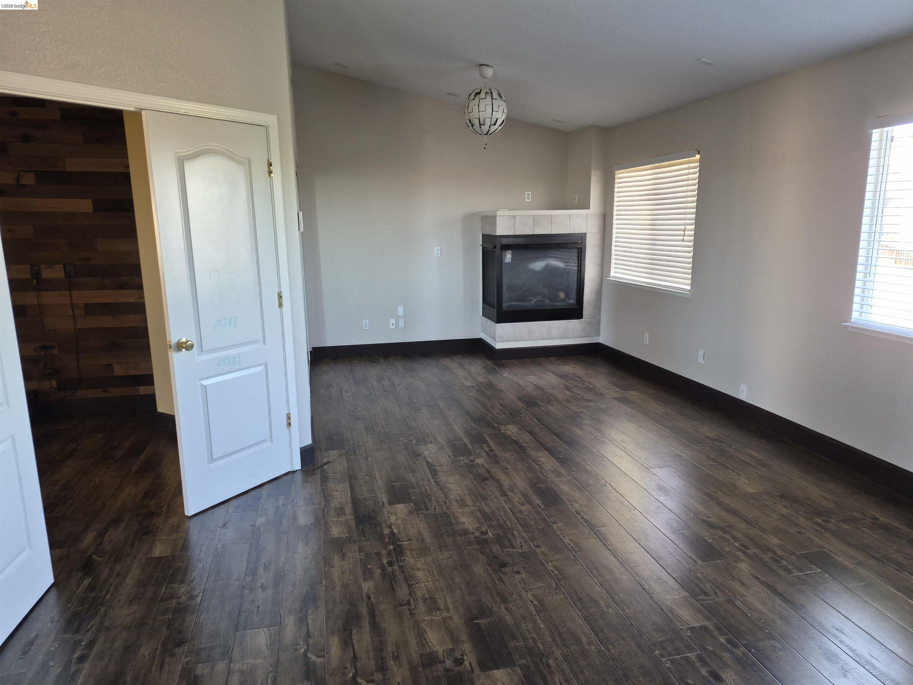 149 Oakpoint Court Bay Point, CA 94565 - Photo 12 of 22 Spacious room featuring wood-finish flooring, a corner-set fireplace with a tiled surround, and multiple windows with horizontal blinds