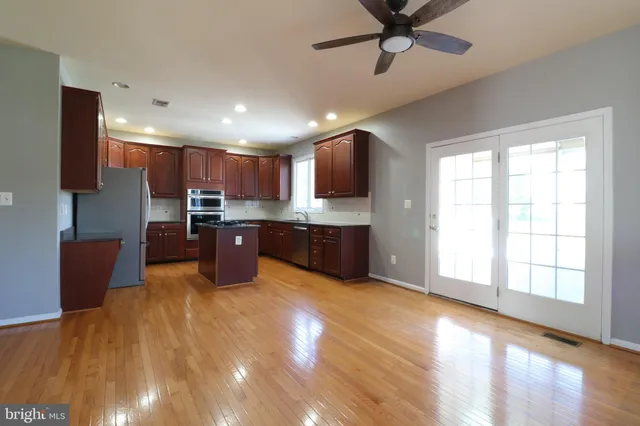 a large kitchen with stainless steel appliances granite countertop a refrigerator a oven a sink with a dining table and chairs with wooden floor