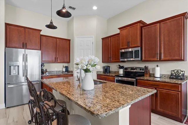 a kitchen with stainless steel appliances granite countertop a refrigerator a stove top oven a sink dishwasher and wooden cabinets with wooden floor