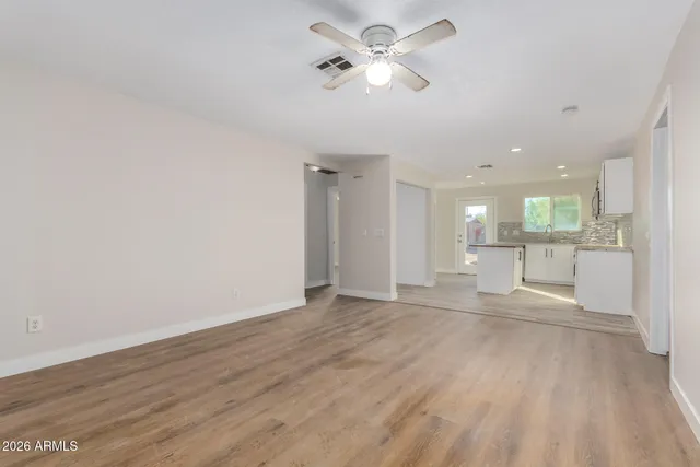 an empty room with wooden floor chandelier fan and windows