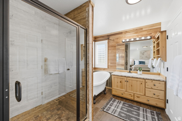 3732 Campbell Road Tooele, UT 84074 - Photo 32 of 69 Bathroom featuring a glass-enclosed shower, freestanding clawfoot tub, wood-finish flooring, wood plank accent walls, and a vanity with natural wood cabinetry and stone-finish countertop