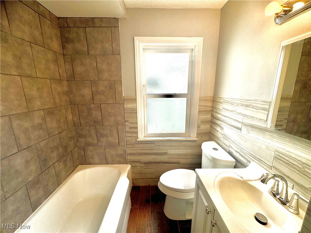 1215 Avondale Road Cleveland, OH 44121 - Photo 20 of 27 Bathroom featuring hardwood / wood-style flooring, tile walls, toilet, vanity, and a tub to relax in