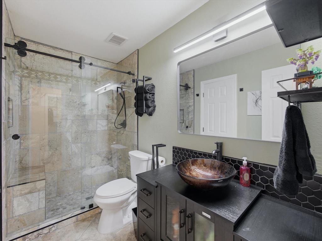 4008 Falcon Ridge Drive Haltom City, TX 76137 - Photo 31 of 40 Modern bathroom featuring a glass-enclosed shower with stone-look tile, a dark wood-finish vanity with a vessel sink, and a black hexagon tile backsplash