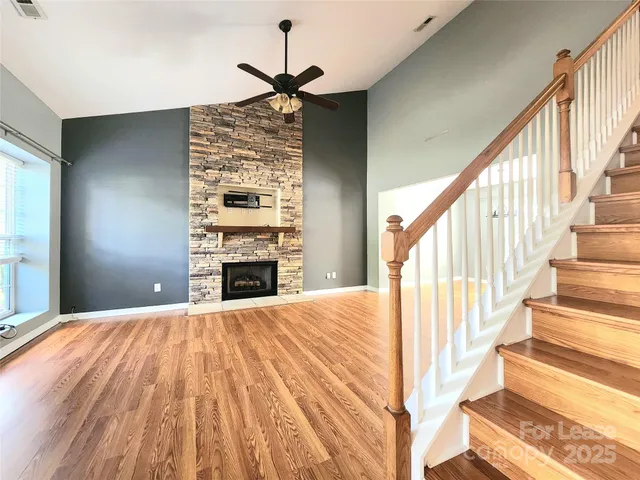 a view of an empty room with wooden floor a ceiling fan and windows