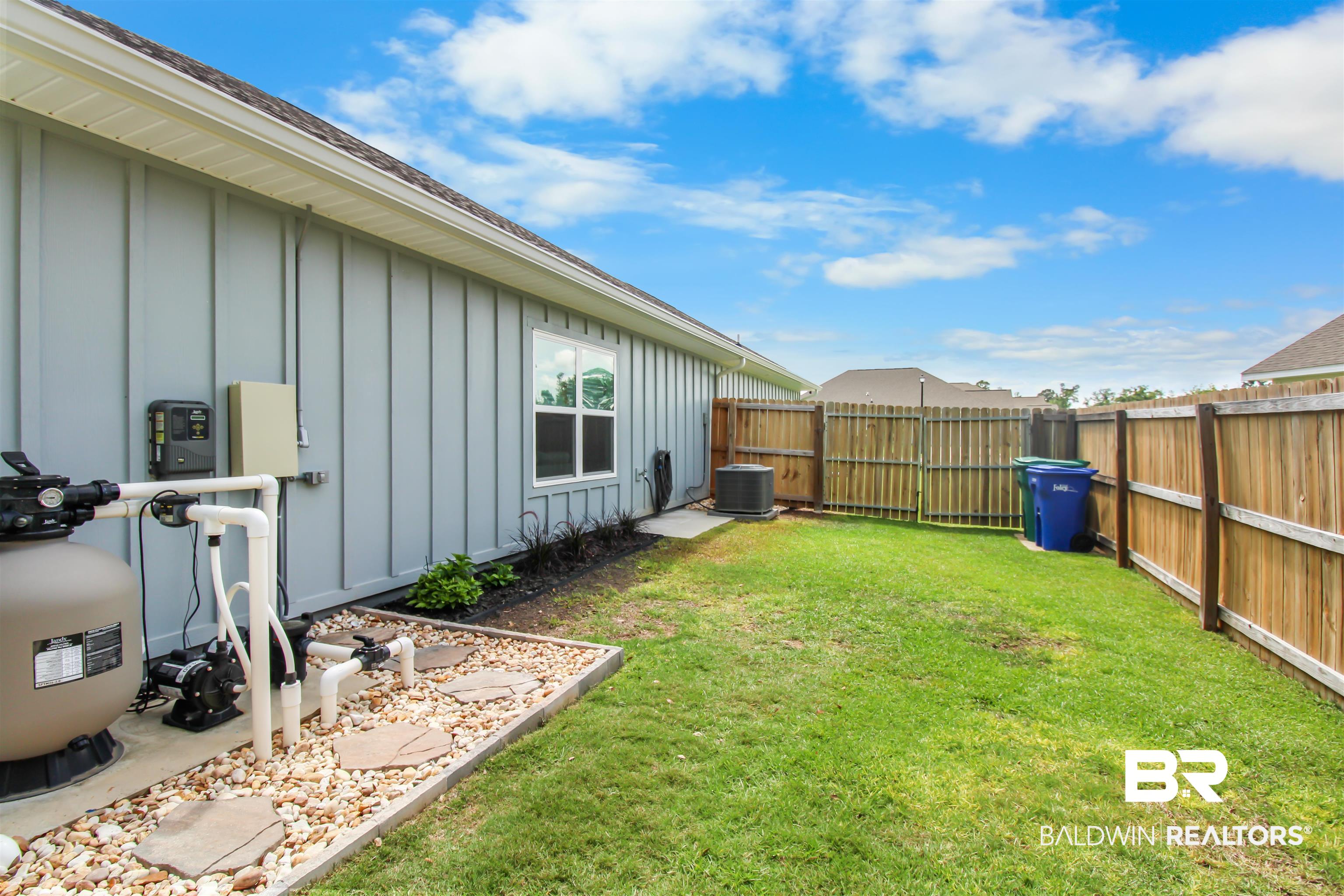 1885 Carly Street Foley, AL 36535 - Photo 35 of 40 Fully fenced backyard with a manicured lawn, a light blue board and batten exterior, and a pool equipment pad with decorative stone
