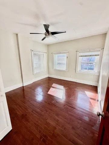 a view of an empty room with wooden floor and a ceiling fan