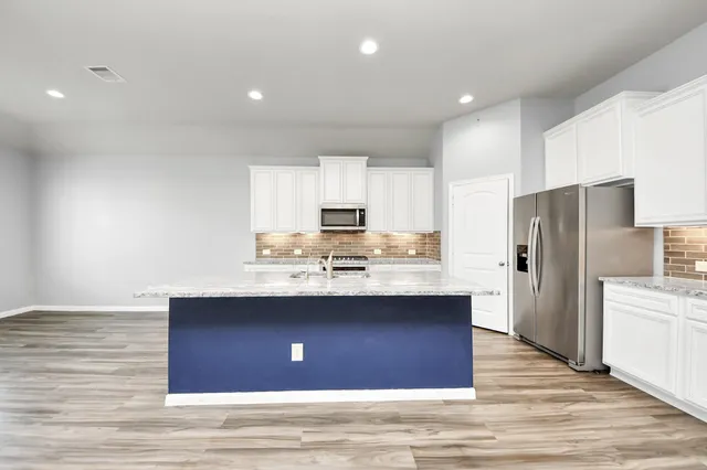 a kitchen with stainless steel appliances granite countertop a stove top oven a sink dishwasher and a refrigerator with wooden floor