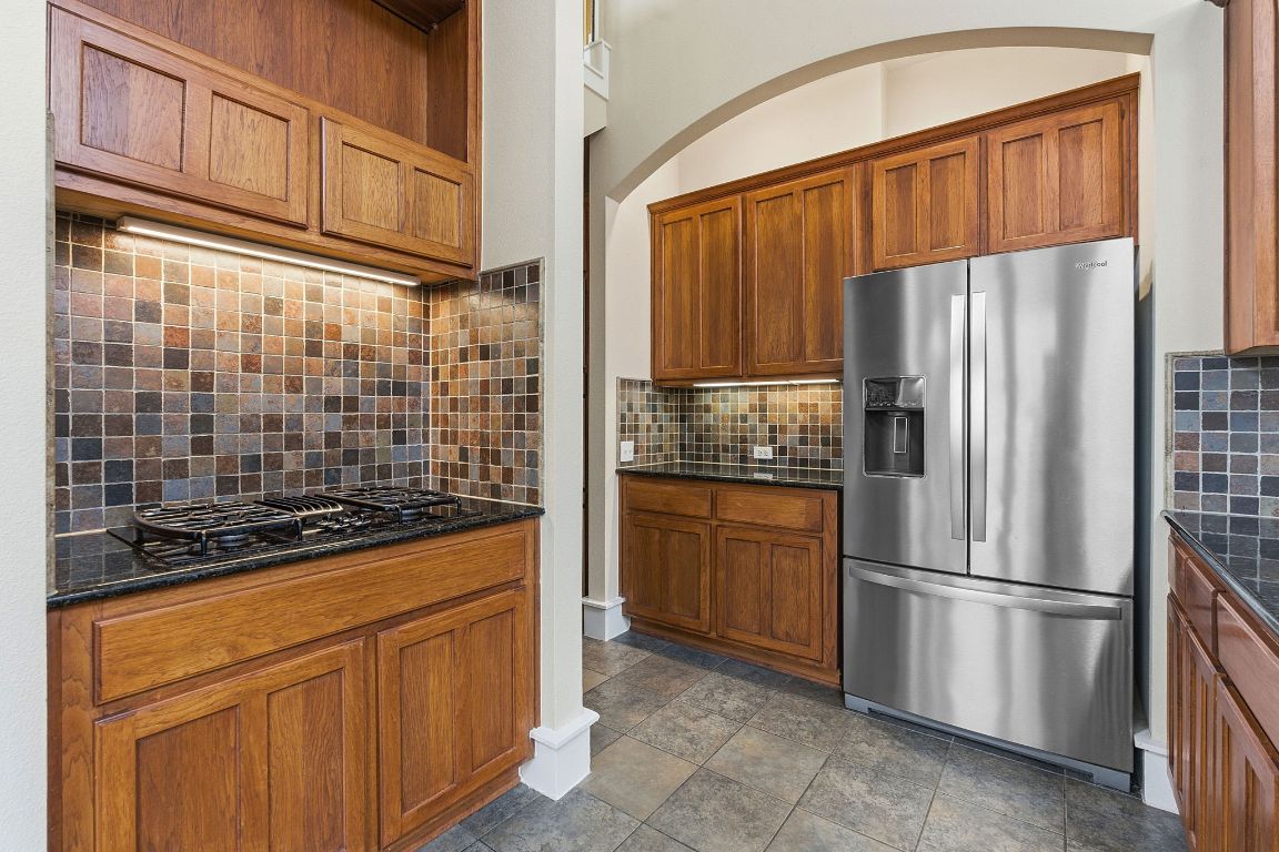 2506 Enfield Road, Unit B Austin, TX 78703 - Photo 16 of 40 Kitchen featuring stainless steel refrigerator with ice dispenser, brown cabinetry, dark stone countertops, and backsplash