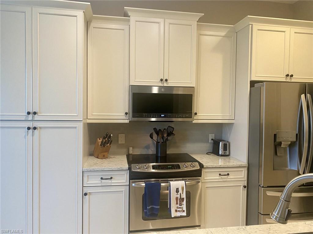 9035 Spring Run Boulevard Estero, FL 34135 - Photo 4 of 9 Kitchen with stainless steel appliances, light stone countertops, white cabinets, and backsplash