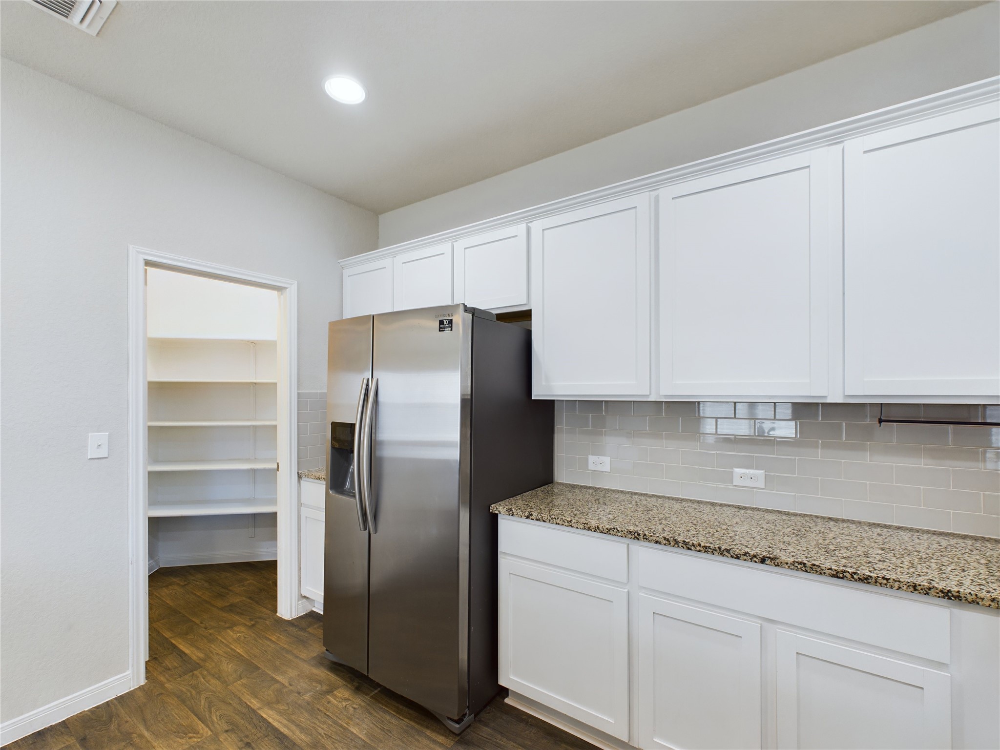 114 Cranbrook Lane Hutto, TX 78634 - Photo 6 of 38 Kitchen with light stone countertops, white cabinetry, stainless steel fridge, and dark hardwood / wood-style flooring