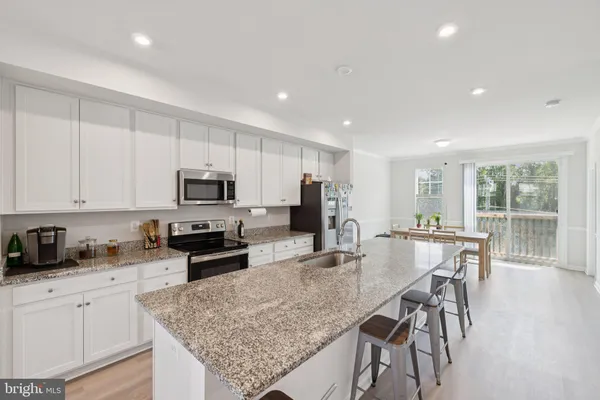 a kitchen with stainless steel appliances granite countertop a stove top oven a sink a refrigerator and white cabinets with wooden floor