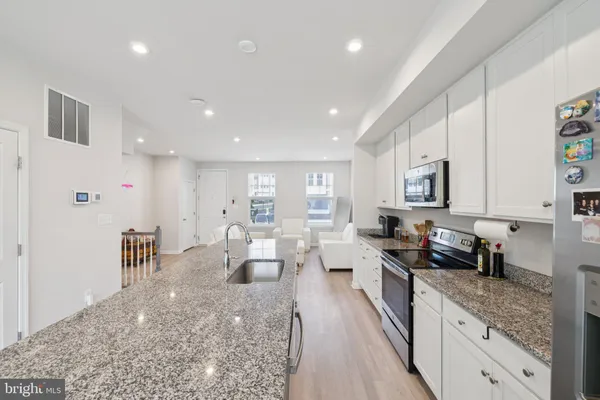 a large kitchen with stainless steel appliances lots of white furniture a window and a granite counter tops