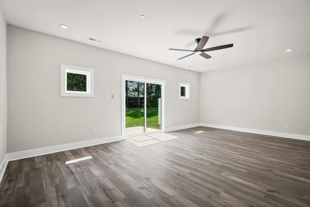 an empty room with wooden floor ceiling fan and windows
