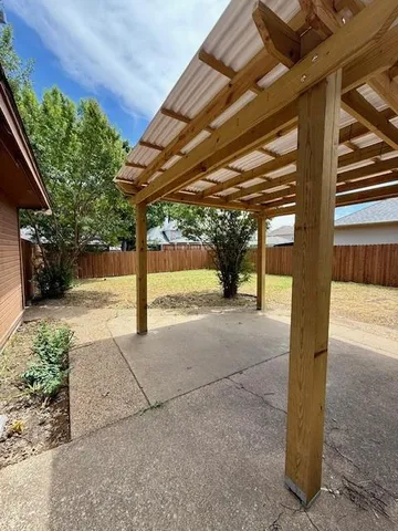 a view of a patio with table and chairs under an umbrella with a small yard