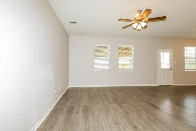 an empty room with wooden floor chandelier fan and windows