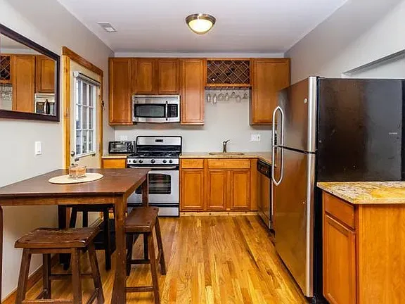 a kitchen with stainless steel appliances granite countertop a stove top oven a sink a dining table and chairs with wooden floor