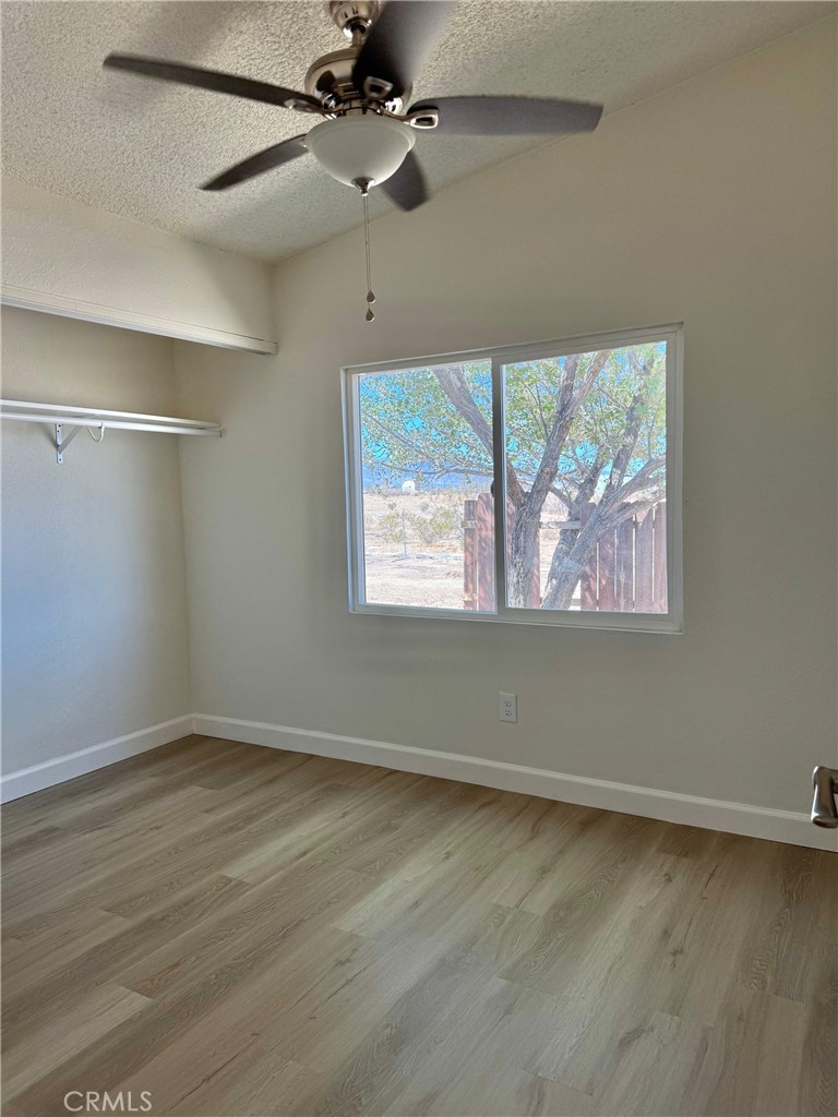 12782 Atsina Road Phelan, CA 92371 - Photo 12 of 18 an empty room with wooden floor ceiling fan and windows