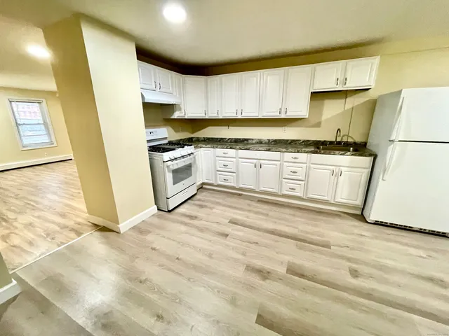 a kitchen with granite countertop a sink a stove a refrigerator and white cabinets