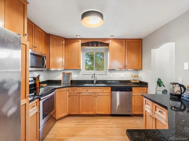 a kitchen with stainless steel appliances granite countertop a sink a stove a refrigerator cabinets and a window
