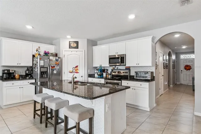 a kitchen with granite countertop a refrigerator a stove a sink dishwasher and white cabinets with wooden floor