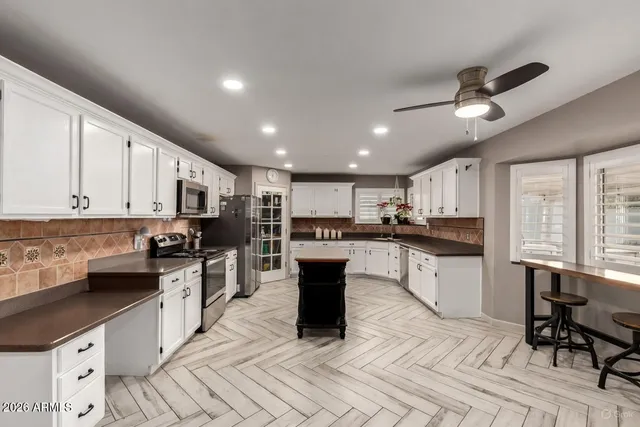 a kitchen with stainless steel appliances kitchen island granite countertop a refrigerator a stove top oven a sink dishwasher and white cabinets with wooden floor