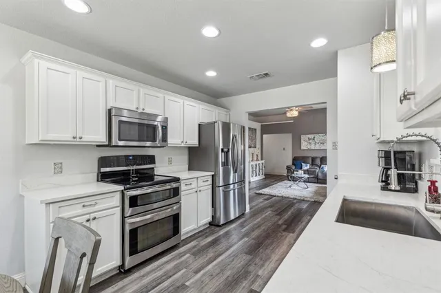 a kitchen with stainless steel appliances granite countertop a refrigerator oven a sink dishwasher and white cabinets with wooden floor