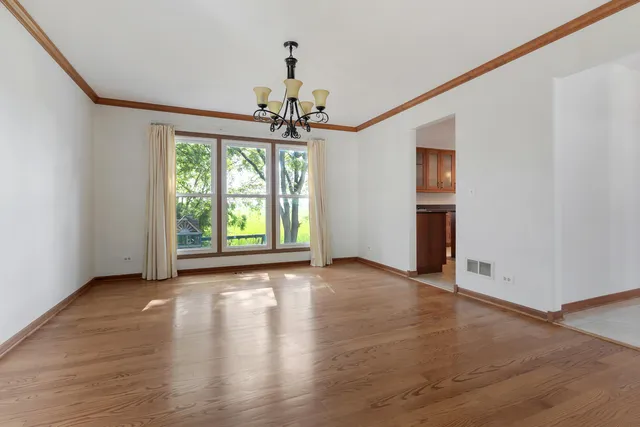 an empty room with wooden floor chandelier and windows