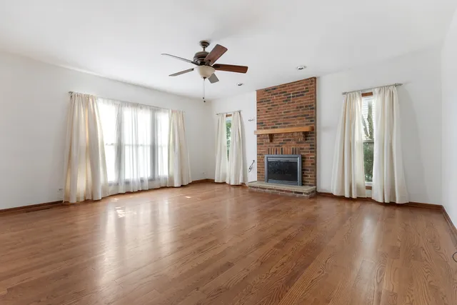 a view of an empty room with wooden floor fireplace and a window